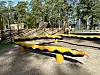 Svart og gult lekeapparat på en utendørs lekeplass med trær i bakgrunnen.